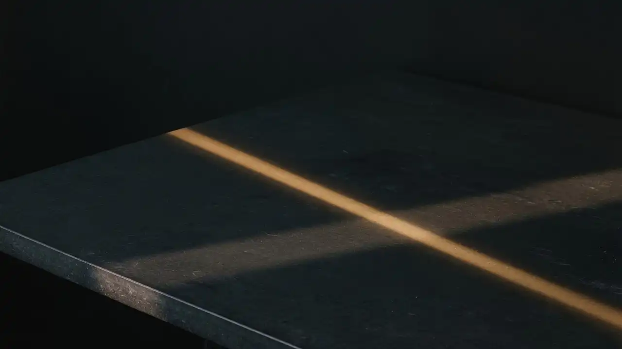 A bare slate desk in low light, with one thin band of warm light across its surface.
